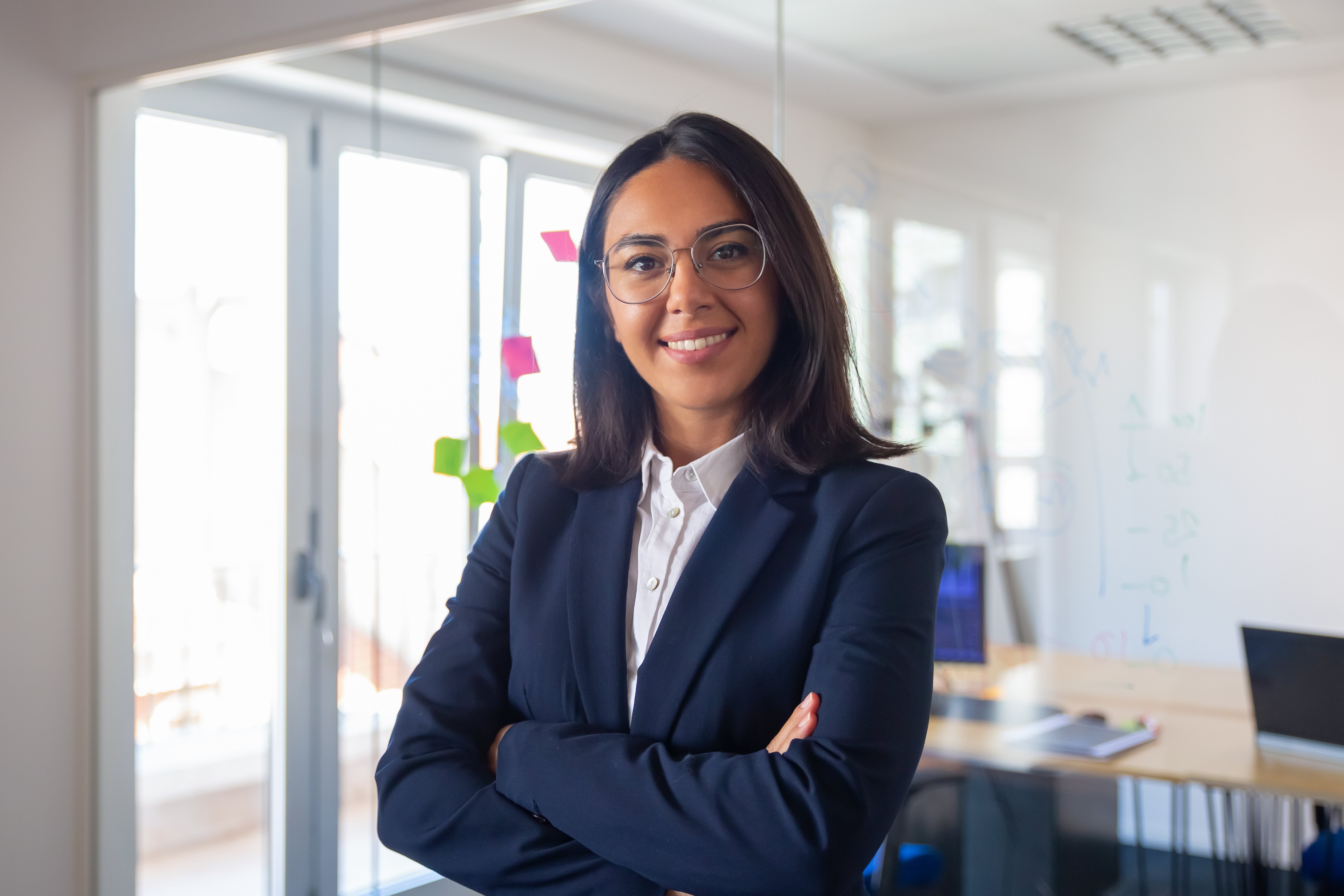 confident-latin-business-leader-portrait-young-businesswoman-suit-glasses-posing-with-arms-folded-looking-camera-smiling-female-leadership-concept