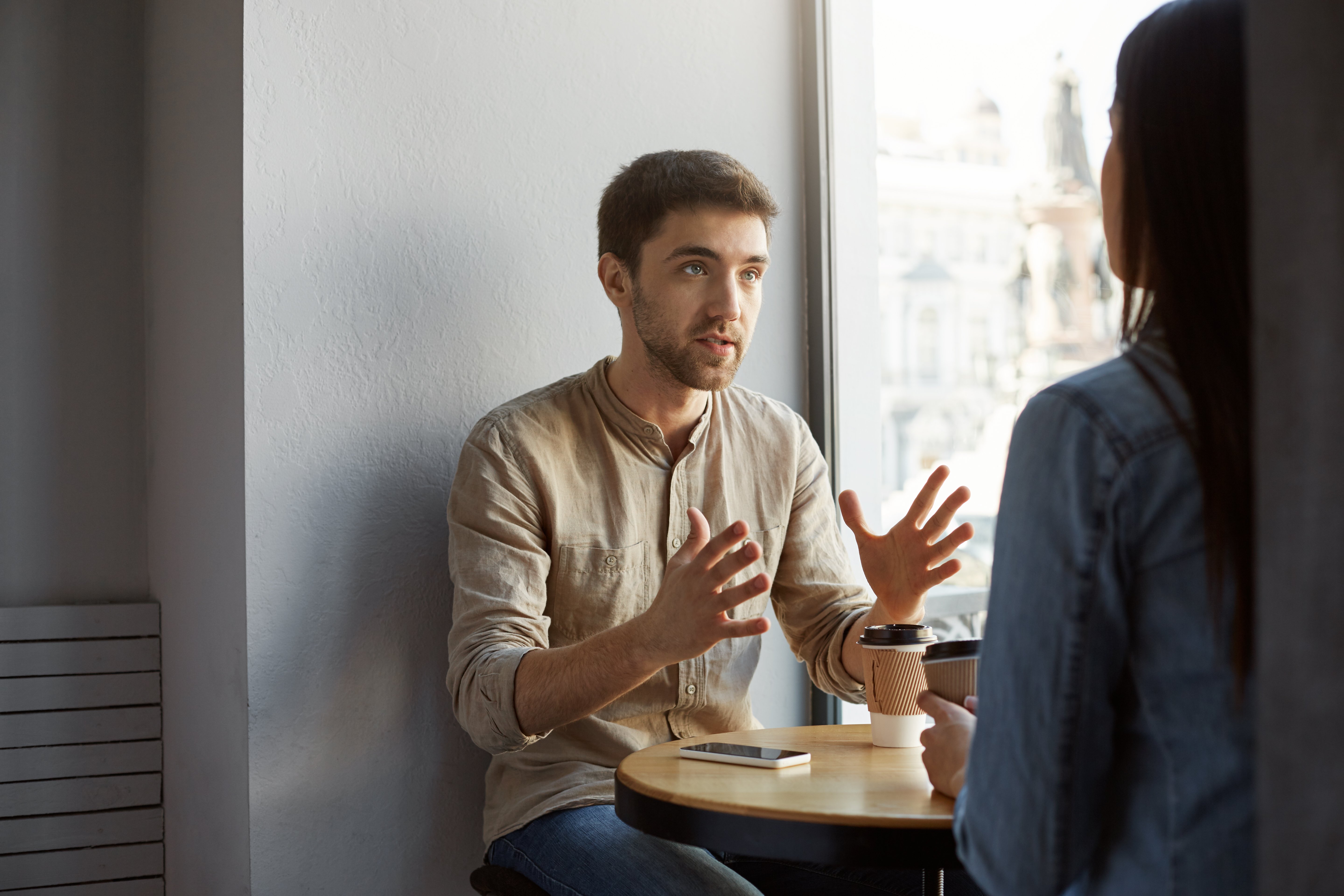 serious-unshaved-dark-haired-man-sitting-cafeteria-with-client-talking-gesticulating-with-hands-trying-make-clear-some-details-commission-he-received