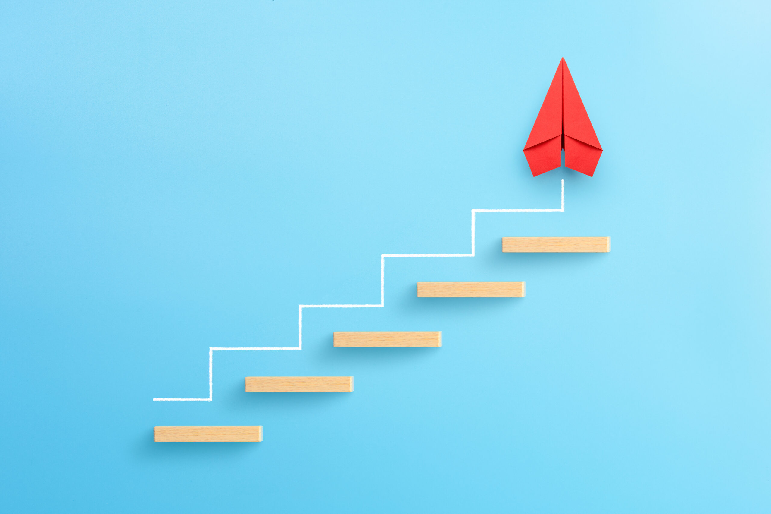 Wooden block stacking as step stair with red paper plane on blue background. [Steps to Creating a Compelling Donor Offer]