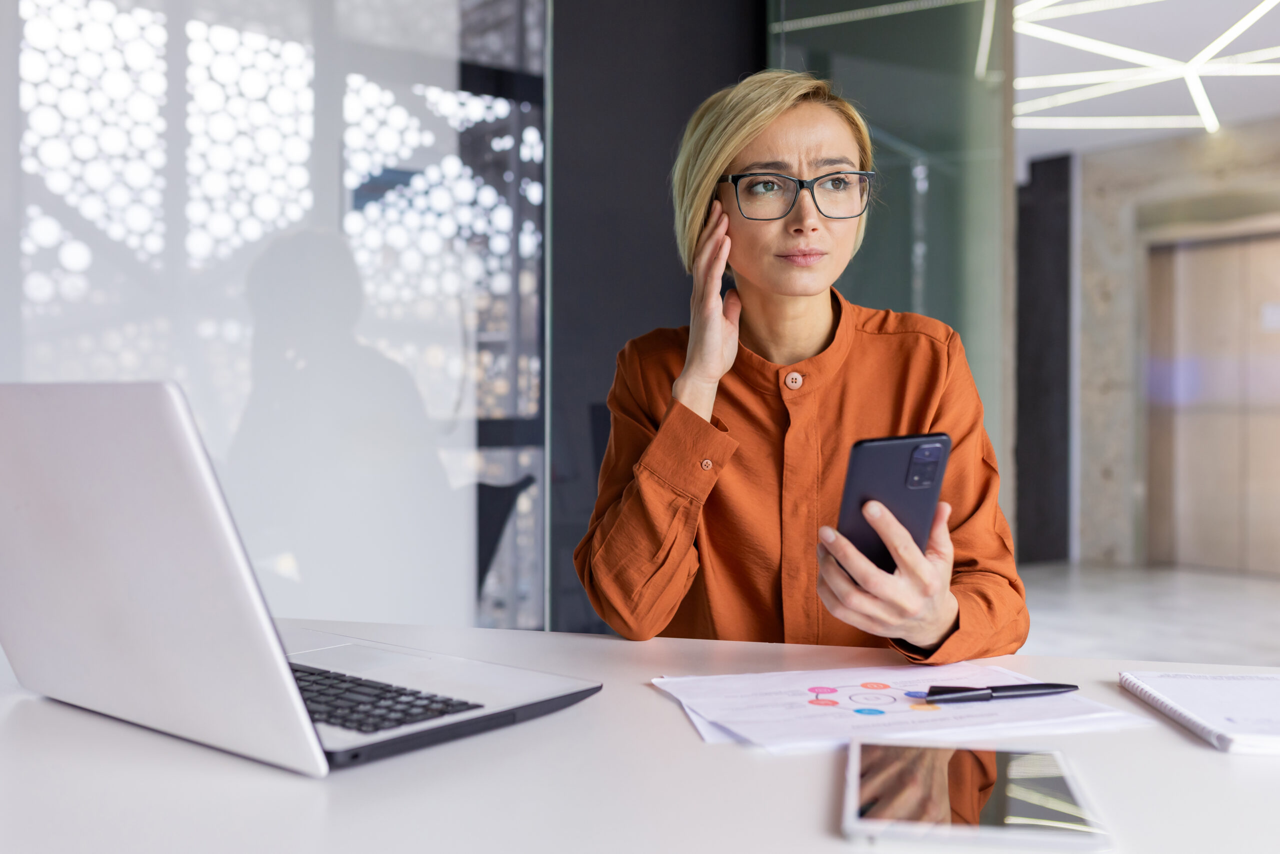 Pensive woman in office holding phone. [Donor Decreases Giving - What Do You Say?]