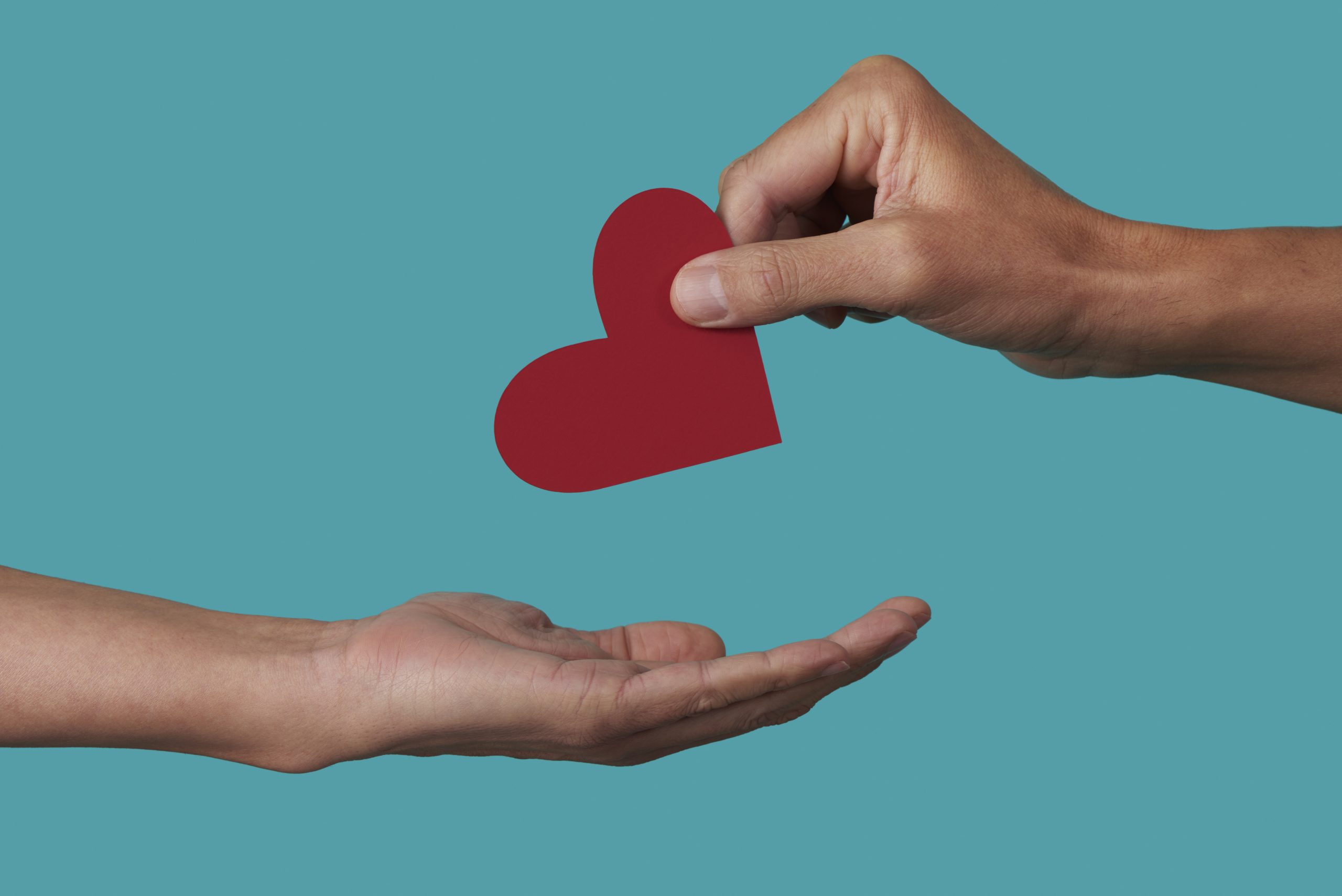 Hand placing a cut-out red heart into another person's open palm.