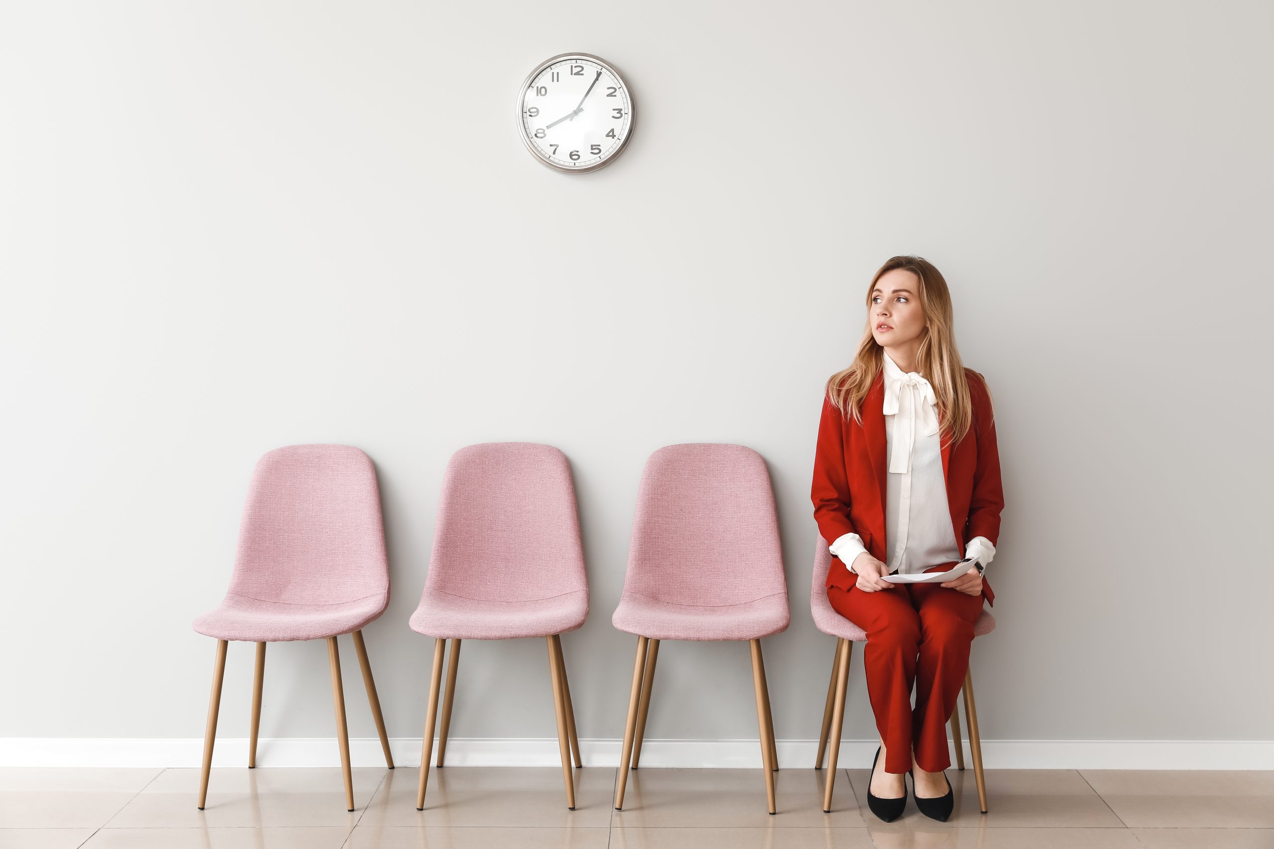 A professional woman is interviewing at a non-profit. She is sitting in a chair in a hallway while waiting for her job interview.