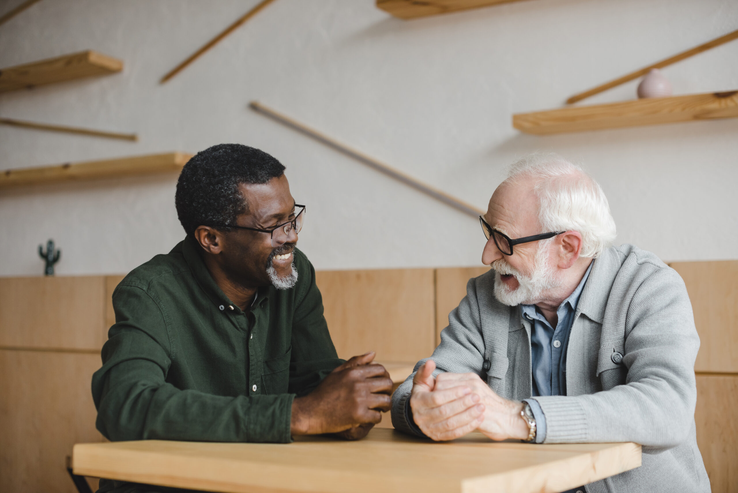 Two men wearing glasses sit at a table while joyfully discussing planned gifts. [Why Your Donor Doesn’t Talk About Their End-of-Life Charitable Plans]