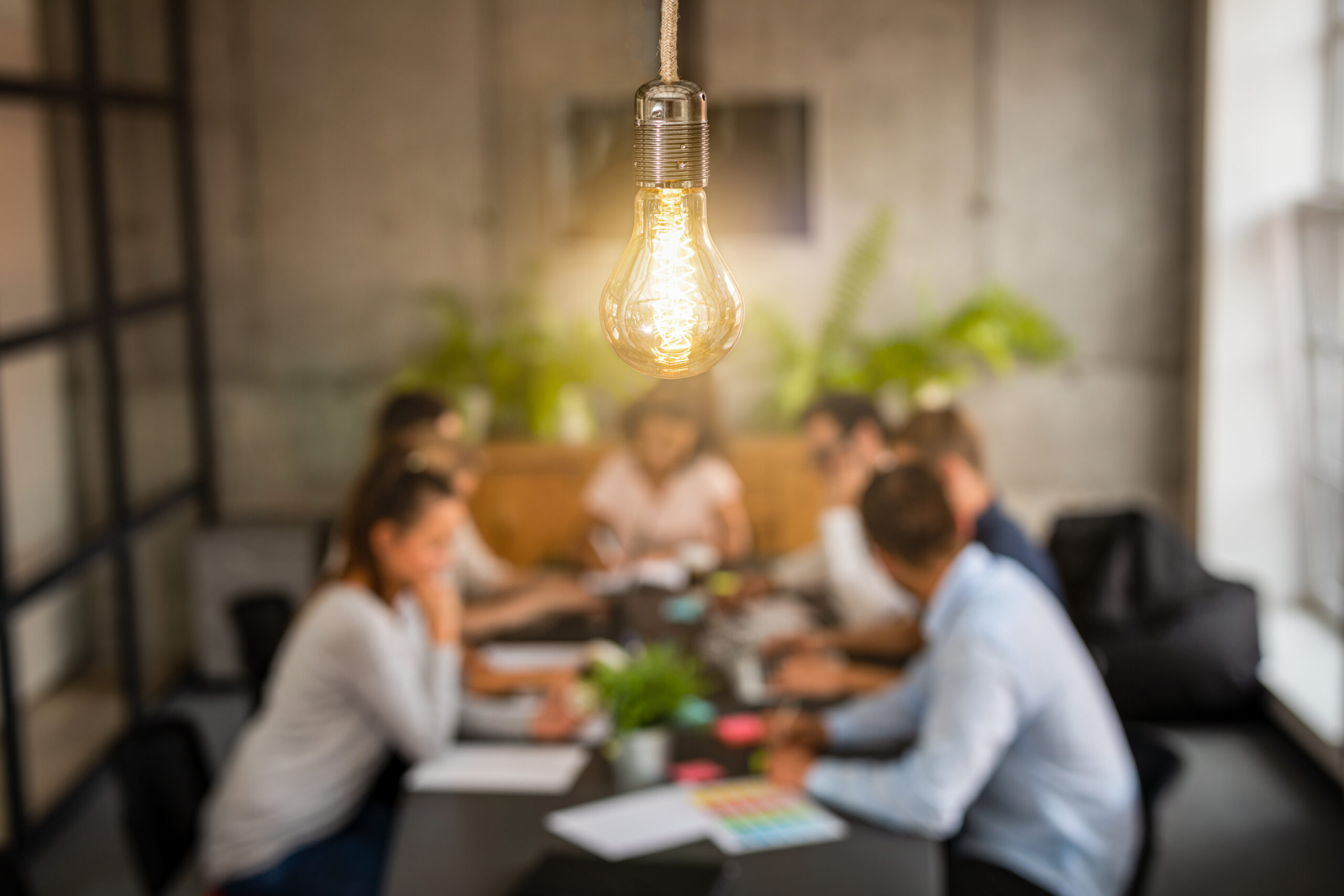A light bulb hangs over a team sitting down for a meeting.