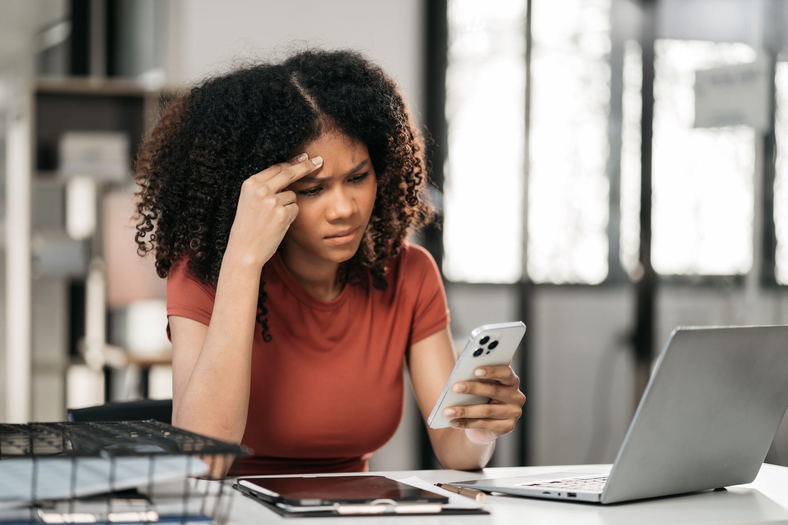 Young business woman is sitting at table, covering her face with her hand and talking on cell phone. [The Reason You Lack Urgency and Courage in Asking]