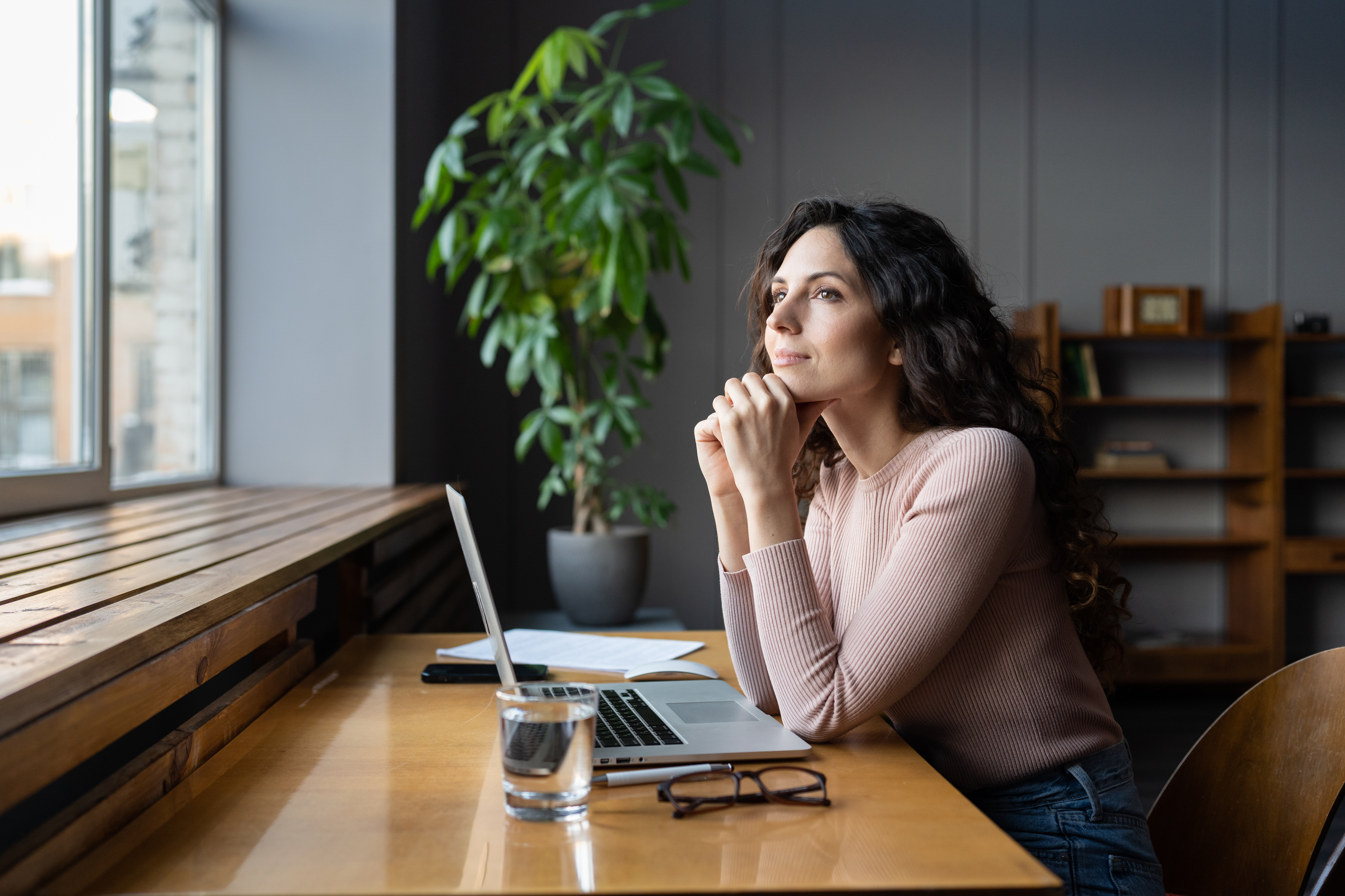 A smiling woman sits in front of her laptop while looking out the window [How to Build Your Learner Muscle for Personal Growth]